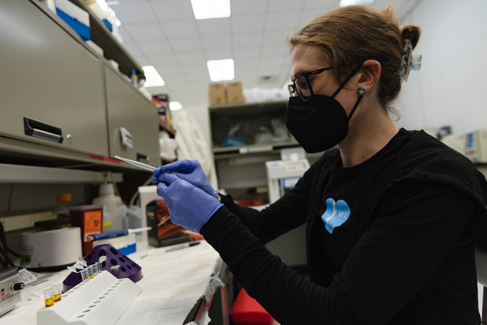 Person in a laboratory setting wearing protective gear and working with equipment.