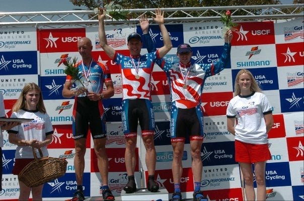 Cyclists on a podium with medals and flowers against a USA Cycling branded backdrop