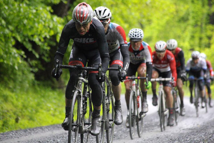 Road cyclists racing on a muddy gravel road with greenery in the background