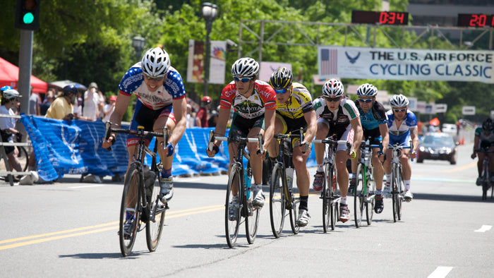 Cycling race with cyclists on a road, spectators, and event signage.