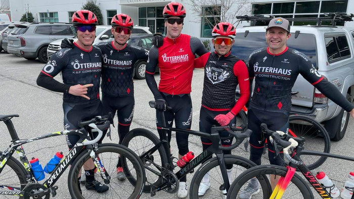 Road cyclists in Otterhaus Coaching kit standing with their bicycles  in a parking lot.