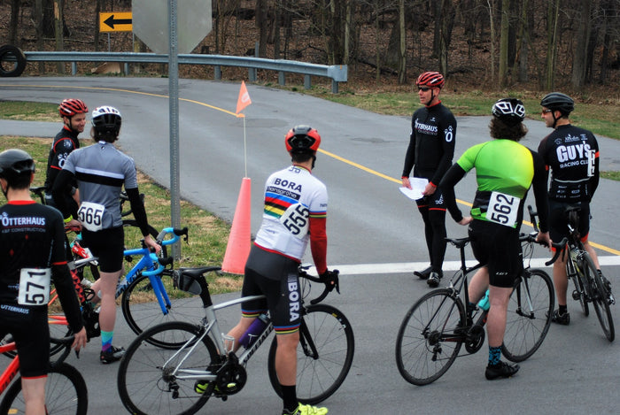 Cyclists preparing for a race on a road with traffic cones and a stop sign.